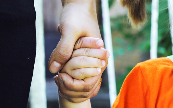Ett barn håller en vuxen i handen. 